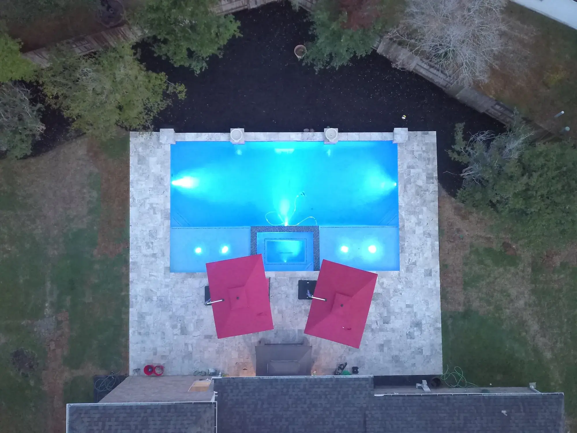Aerial drone view of a custom in-ground pool and attached spa with travertine decking in a Houston-area backyard built by Sam Houston Pools and Outdoors