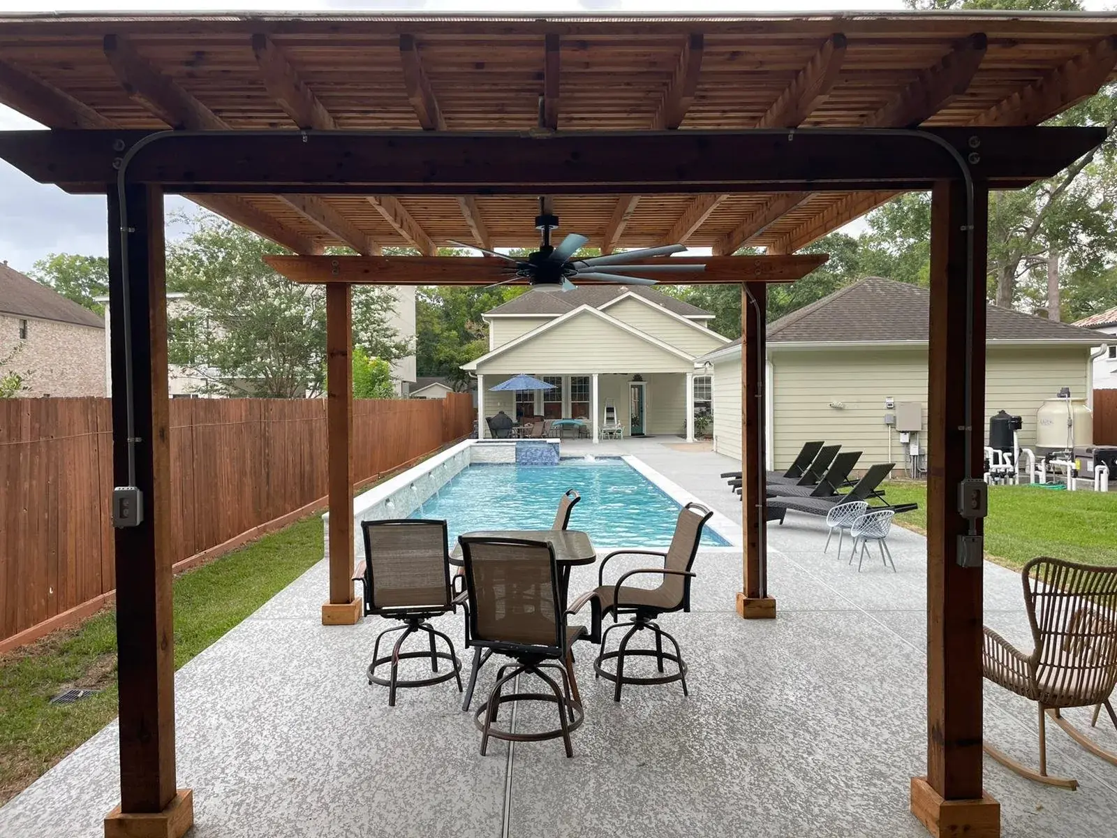 Cedar pergola providing shade over a poolside patio with outdoor seating in East Texas