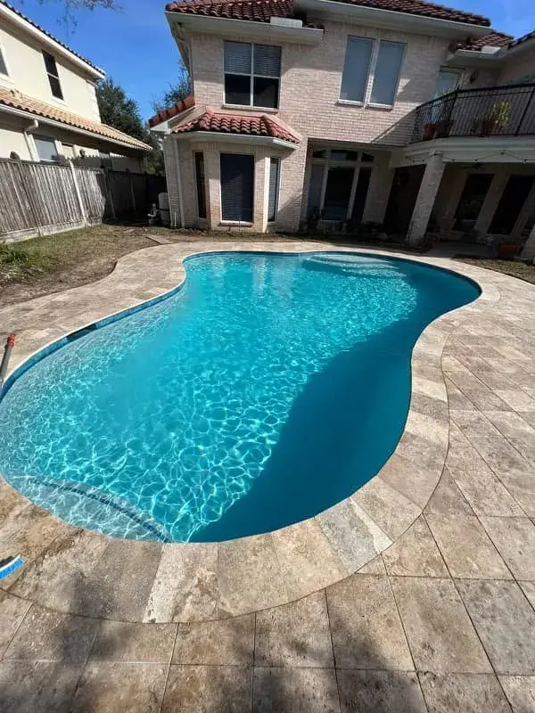 Freeform curved swimming pool with travertine pool deck and lush landscaping in East Texas