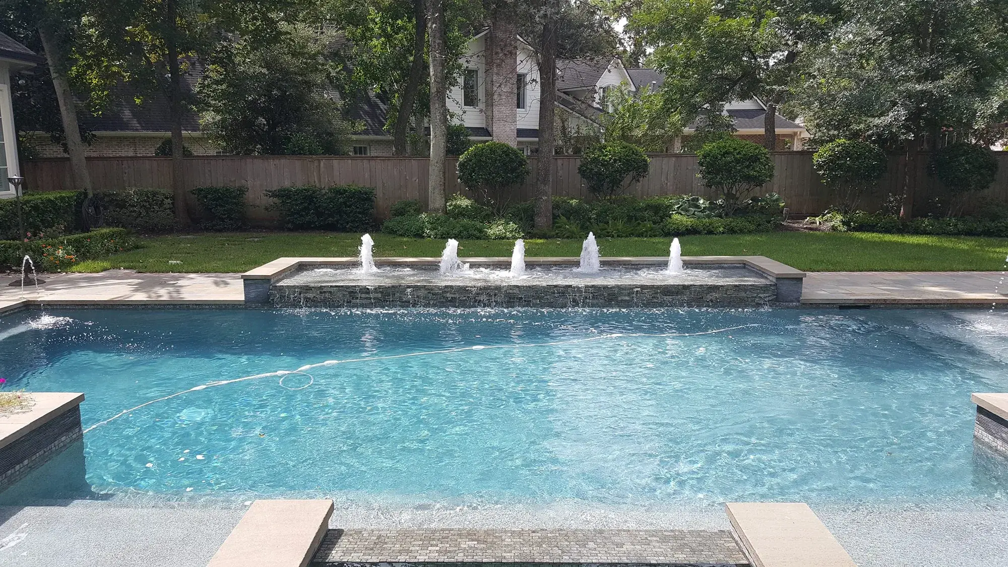 Geometric pool with deck bubblers and a raised water feature wall in an East Texas custom build