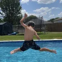 Child jumping into a backyard swimming pool on a summer day in a Houston-area home
