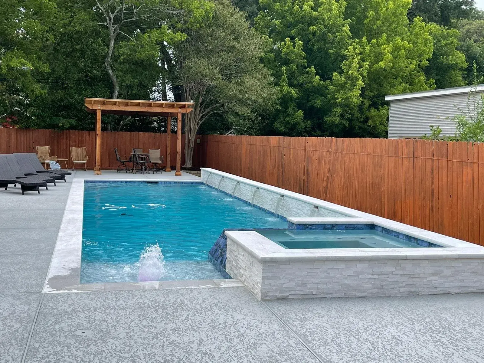 Modern pool and spa combination with a stacked stone waterfall feature, built by Sam Houston Pools and Outdoors