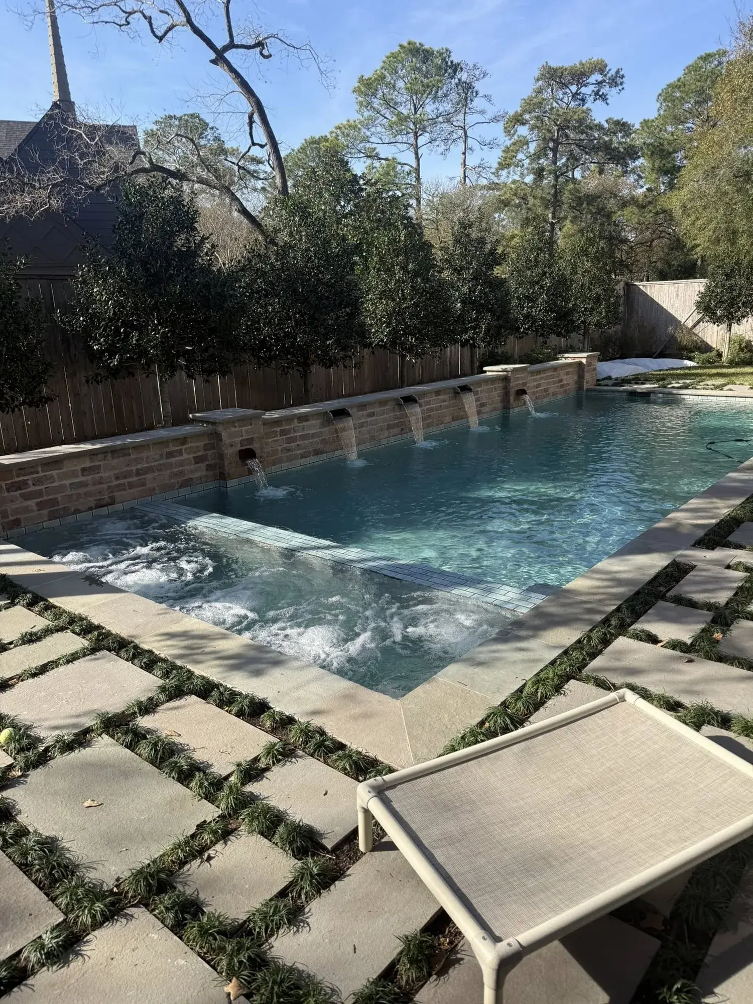 Modern rectangular pool with three sheer descent waterfalls cascading from a raised wall in a Houston-area backyard